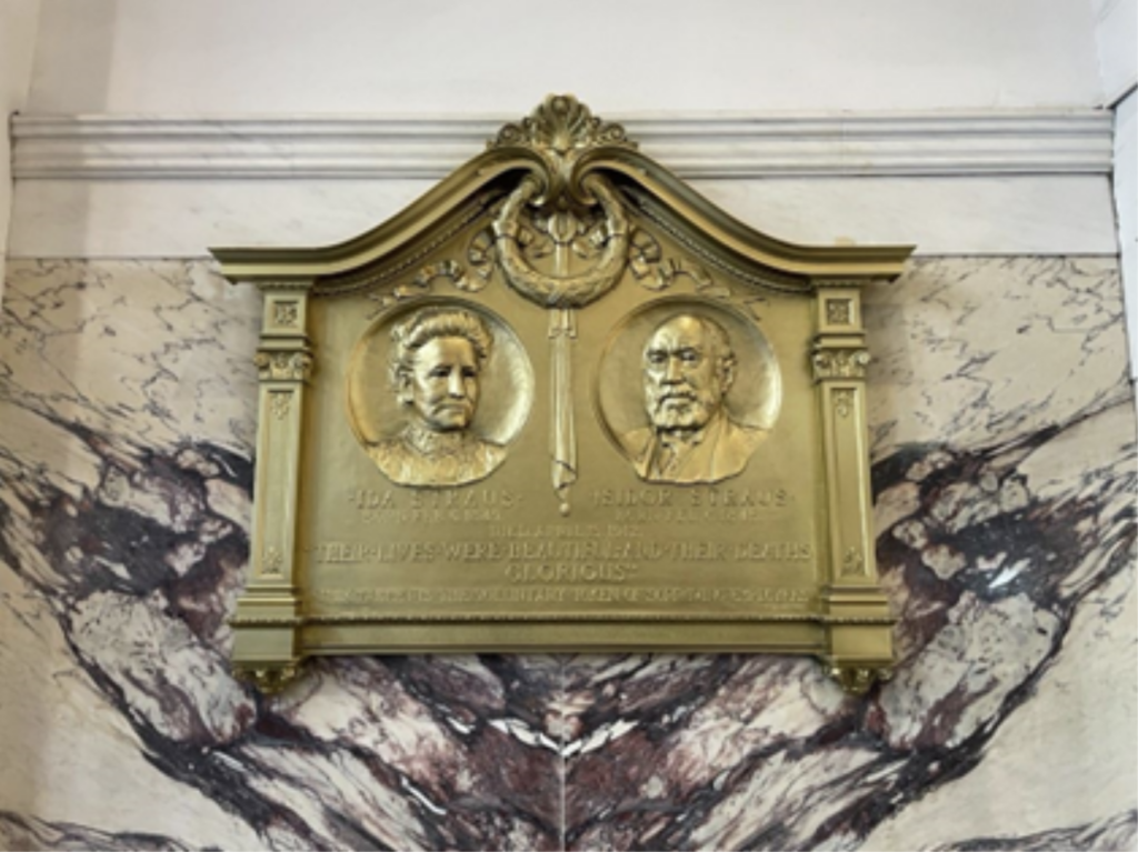 A large, ornate bronze plaque is attached to an enormous piece of granite on the wall inside Macy’s department store in Manhattan.